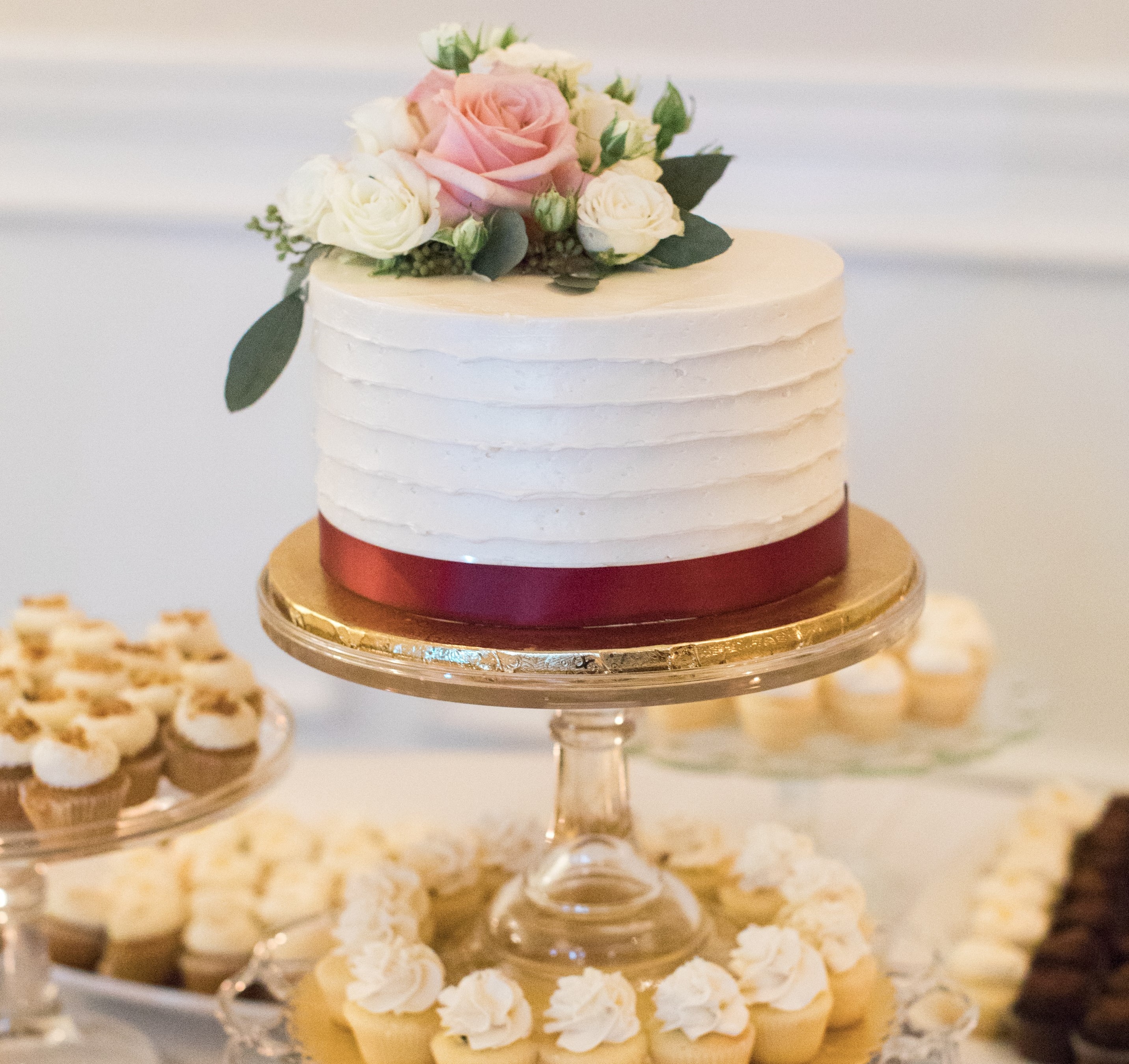 flower decorated cake on a platter with mini cupcakes image